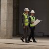 Business People Discussing Investment at Construction Site Full length portrait of two business people wearing hardhats and holding plans while walking at construction site indoors, copy space