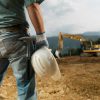 closeup back view of male engineer standing on construction site holding white hardhat